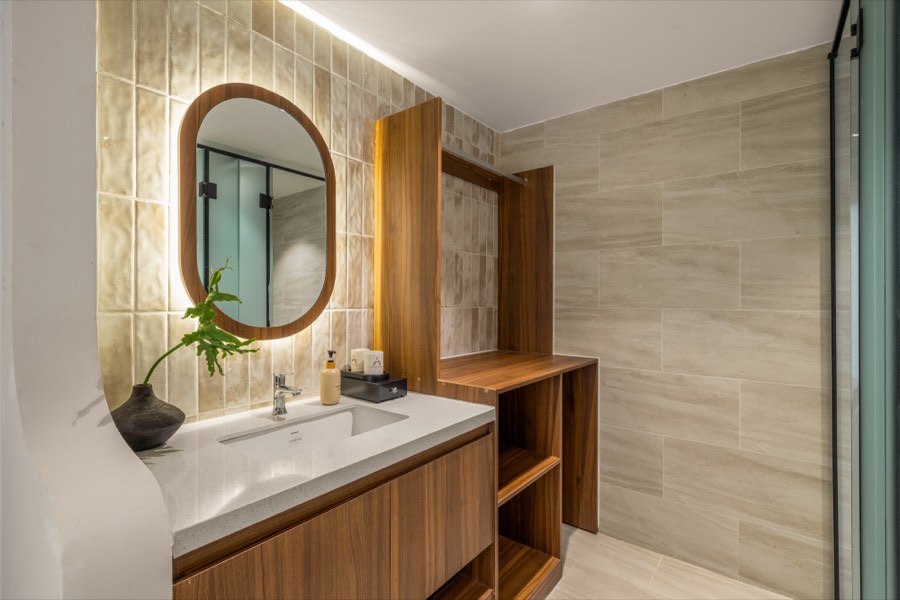 Bathroom with a backlit oval mirror, walnut vanity and glazed tile