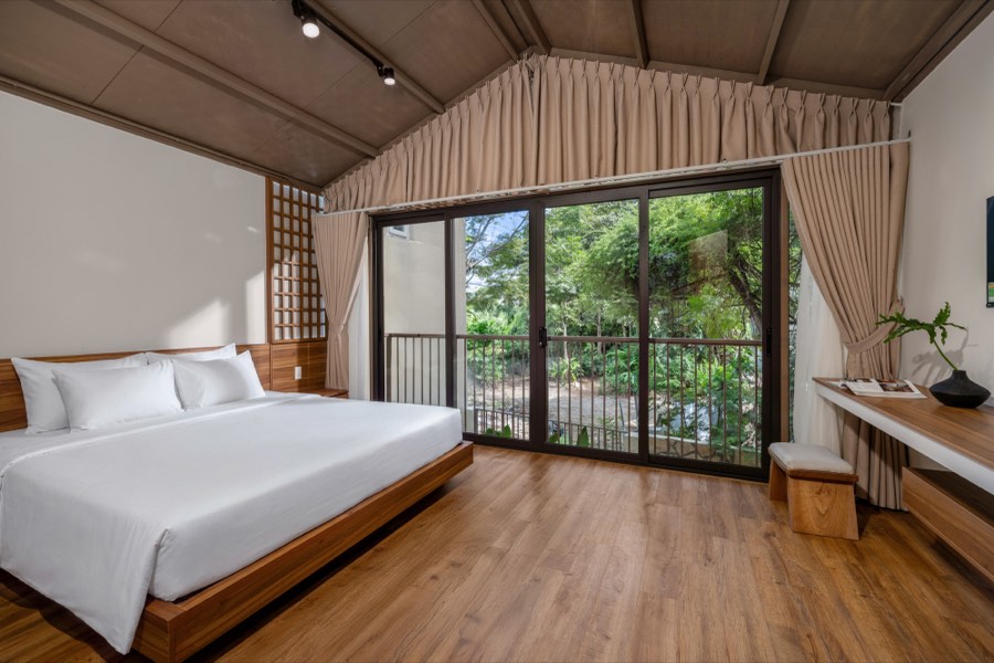 Bedroom One — a king bed on a timber platform facing a balcony full of green