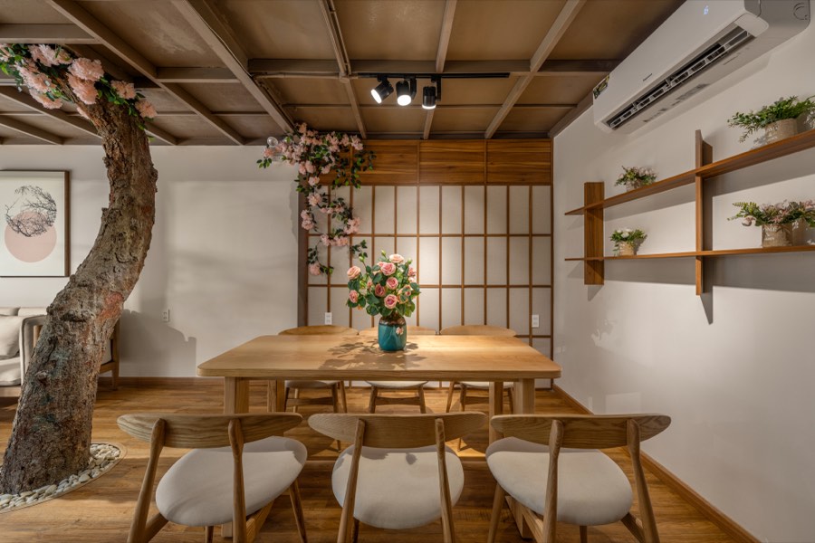 Six chairs around solid ash, shelves of ferns behind — dining room at Fuka House, Da Nang