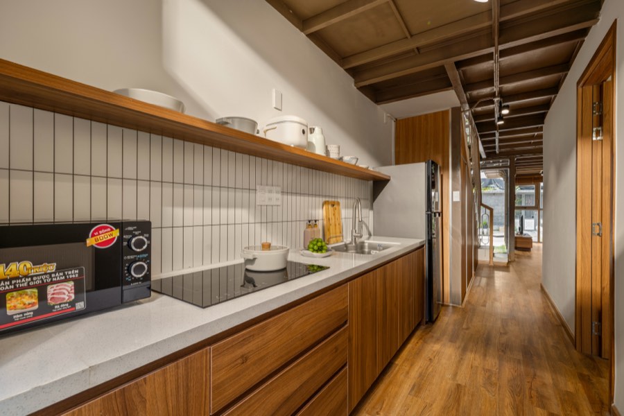 Induction hob, stone counter and an open walnut shelf — kitchen at Fuka House, Da Nang