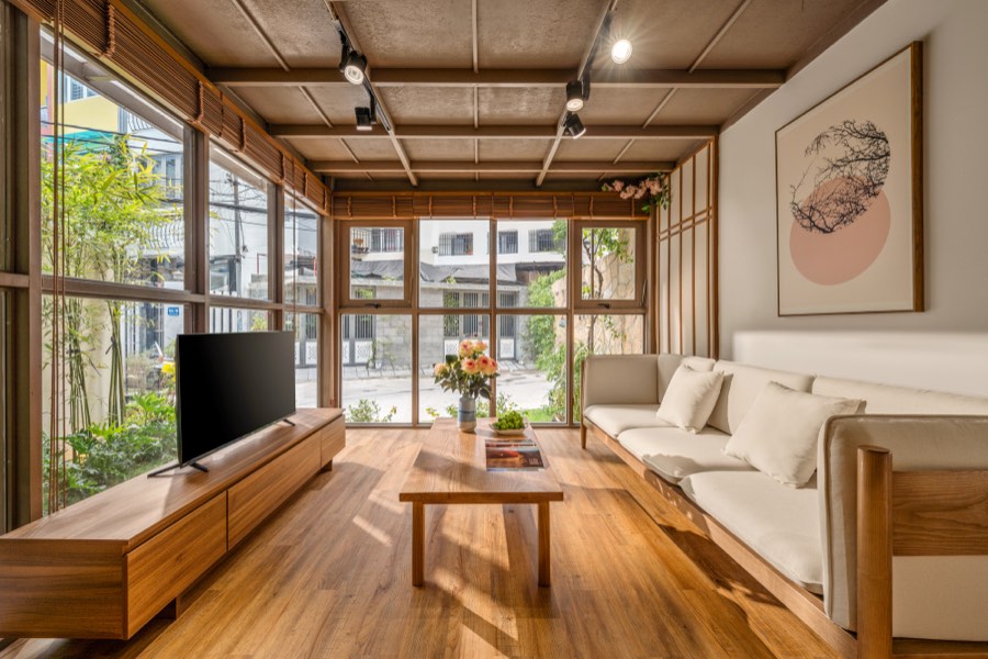 A long sofa facing the garden, under the coffered timber ceiling — living room at Fuka House, Da Nang