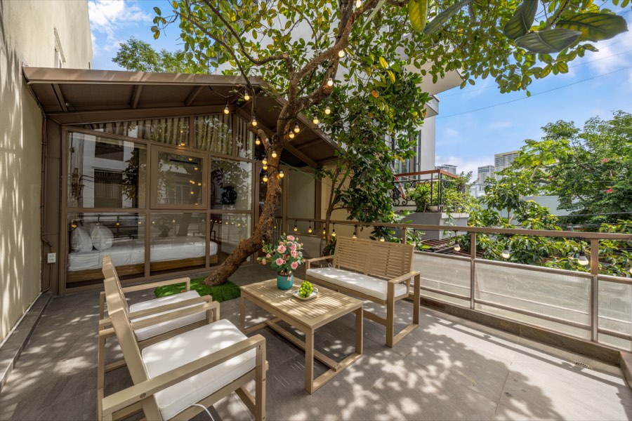 Second-floor terrace with slatted furniture beneath a tree hung with lanterns